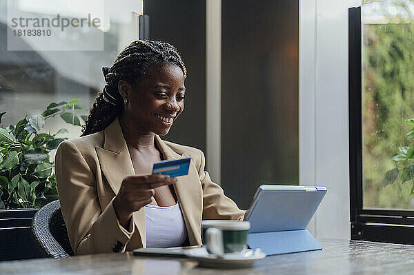 Glückliche Geschäftsfrau hält Kreditkarte in der Hand und nutzt Tablet-PC im Café