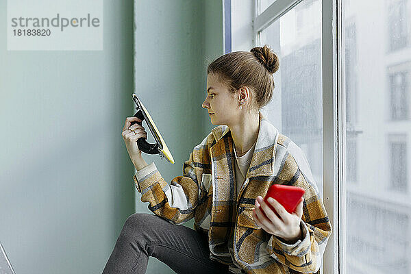 Junge Frau mit Smartphone schaut in der Wohnung auf Arbeitsgerät