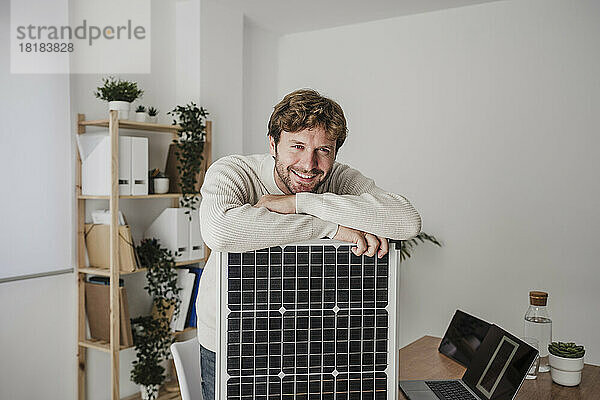 Glücklicher Geschäftsmann stützt sich im Büro auf Solarpanel
