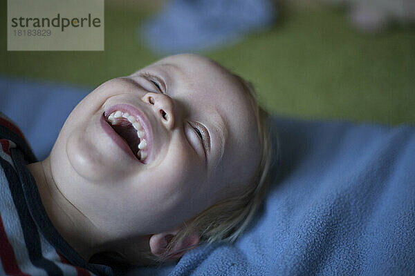 Portrait of laughing little boy lying on bed