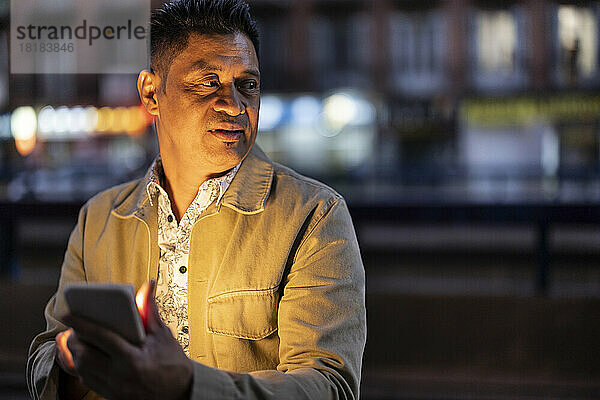 Reifer Mann hält nachts Smartphone in der Hand
