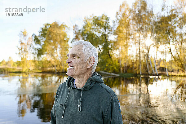 Glücklicher älterer Mann mit Kapuzenshirt vor dem See