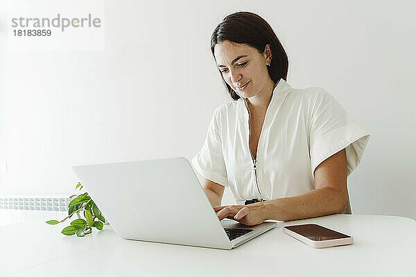Lächelnde Geschäftsfrau  die zu Hause einen Laptop auf dem Tisch benutzt