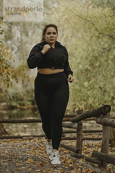 Entschlossene übergewichtige junge Frau joggt im Herbstpark