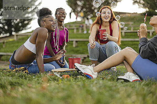 Glückliche Frau bläst Seifenblasen mit Freunden und genießt den Park