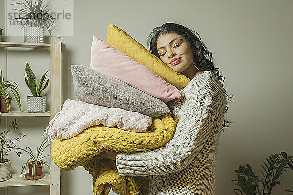 Woman with eyes closed carrying pillows and blankets at home