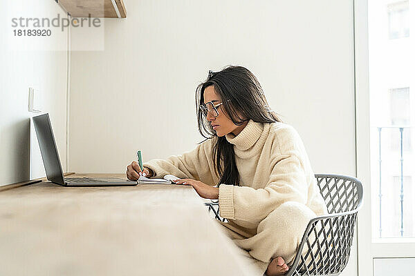 Junge Frau schreibt Tagebuch und arbeitet im Heimbüro
