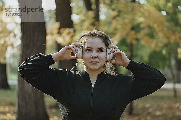 Lächelnde junge Frau  die im Park Musik über kabellose Kopfhörer hört