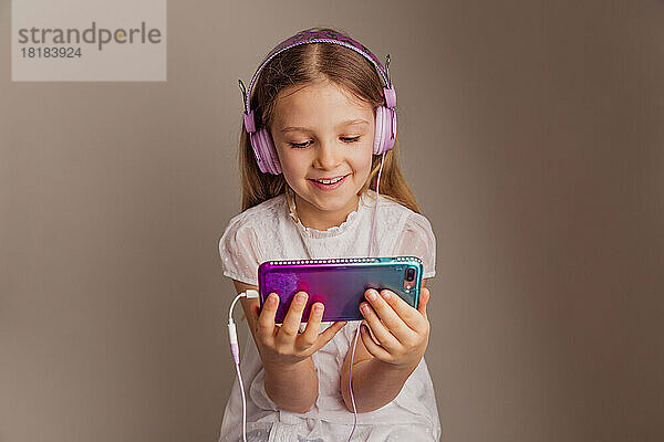 Porträt eines lächelnden Mädchens  das sich mit Smartphone und Kopfhörern einen Film ansieht