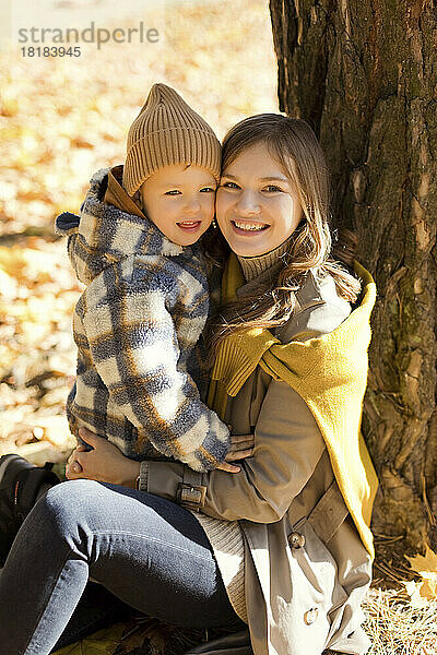Glückliche Mutter und süßer Junge sitzen neben Baum im Park