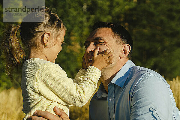 Glückliches Mädchen berührt an einem sonnigen Tag die Wangen seines Vaters auf dem Feld
