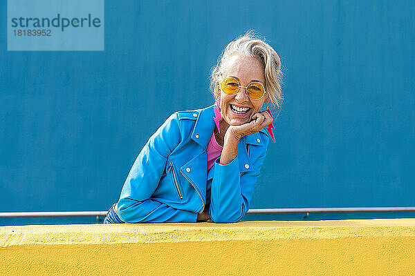 Glückliche Frau mit Sonnenbrille vor blauer Wand
