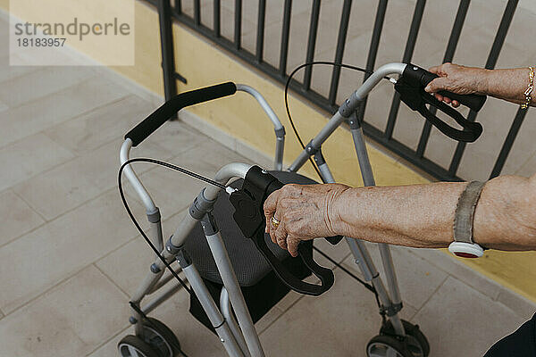Hände einer älteren Frau halten Gehhilfe auf Fußweg