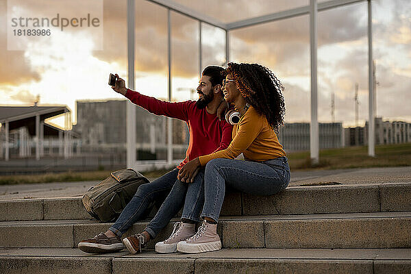 Glückliche junge Frau mit ihrem Freund  die bei Sonnenuntergang ein Selfie per Smartphone macht