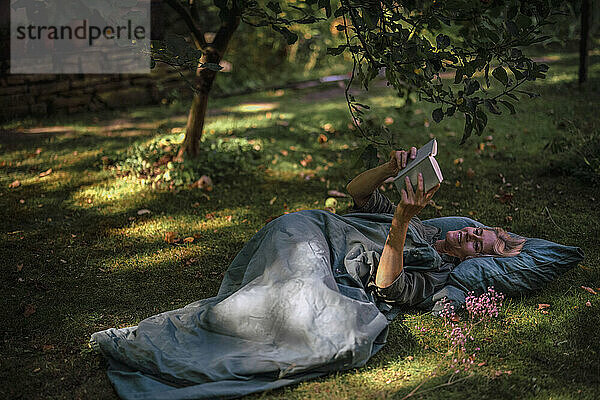 Mature woman reading book lying on grass in garden