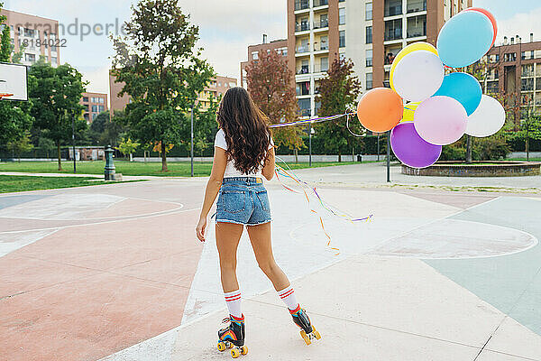 Junge Frau mit bunten Luftballons beim Rollschuhlaufen auf dem Sportplatz