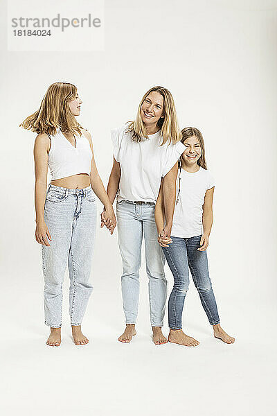 Happy mother and daughters holding hands against white background