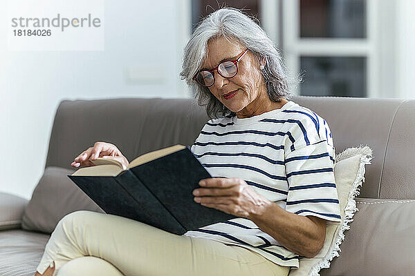 Ältere Frau mit Brille liest zu Hause ein Buch