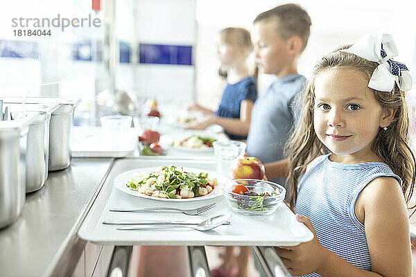 Girl holding food tray standing in school cafeteria