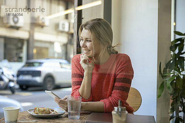 Glücklicher Freiberufler  der mit dem Smartphone im Café beim Essen sitzt