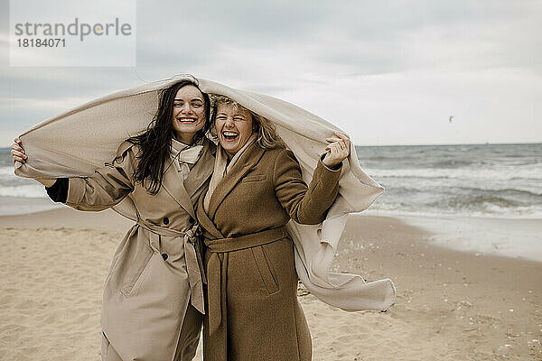 Happy mother and daughter with blanket standing at beach