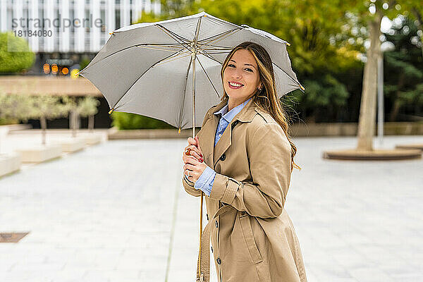 Glückliche Geschäftsfrau hält Regenschirm auf Fußweg