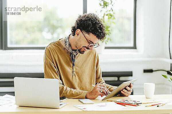 Glücklicher Illustrator mit Brille und digitalem Tablet am Schreibtisch