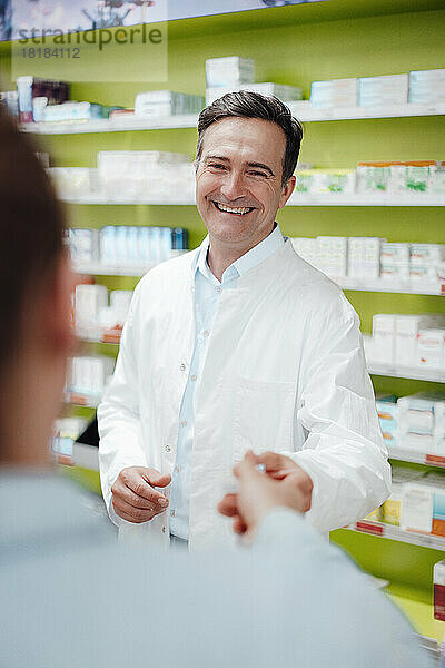 Glücklicher Apotheker  der dem Kunden im Geschäft Medikamente gibt