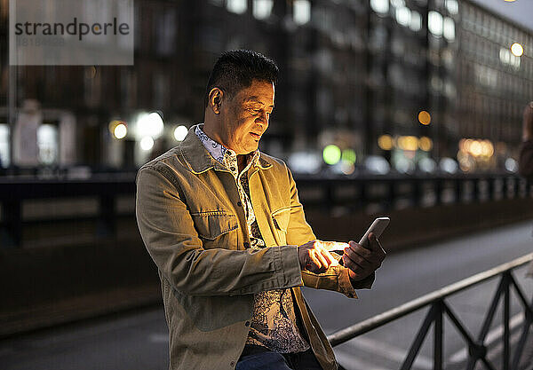 Reifer Mann sitzt auf Geländer und benutzt Smartphone