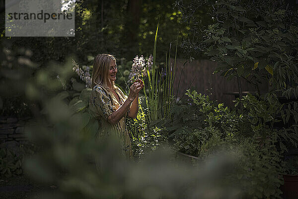 Lächelnde Frau betrachtet Pflanze im Garten