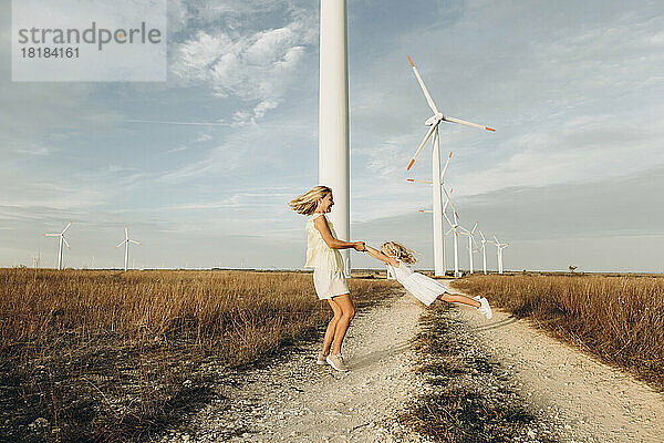 Fröhliche Mutter spinnt Tochter vor Windkraftanlagen