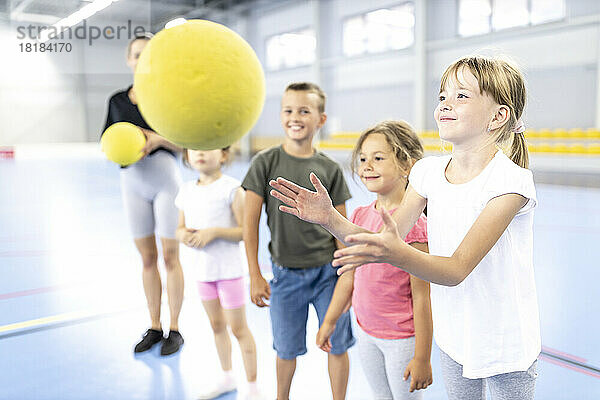 Lächelndes Mädchen fängt Ball mit Freunden auf dem Schulsportplatz