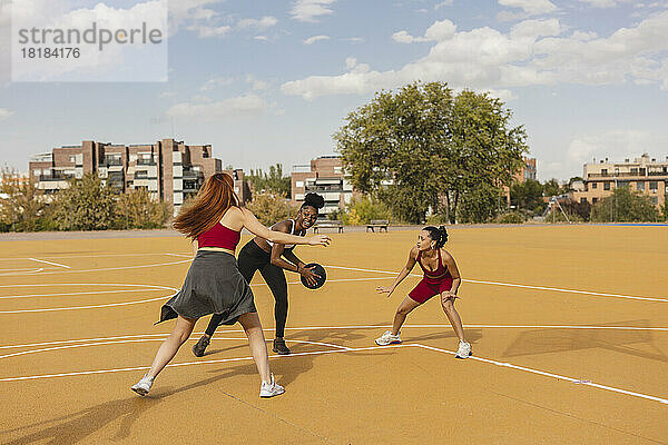 Junge Frau übt Basketball mit Freunden auf dem Sportplatz