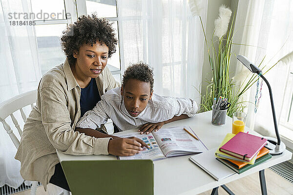 Mutter unterstützt Sohn beim E-Learning per Laptop auf dem heimischen Tisch