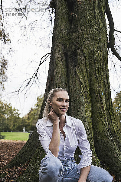 Nachdenkliche Frau kauert vor einem Baum im Park