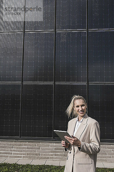 Glückliche Geschäftsfrau steht mit Tablet-PC vor Sonnenkollektoren