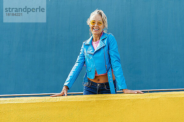 Glückliche reife Frau mit Sonnenbrille vor blauer Wand