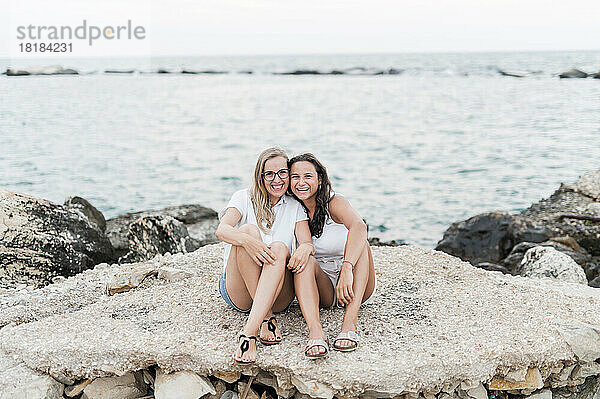 Fröhliche Freunde sitzen zusammen auf einem Felsen am Strand
