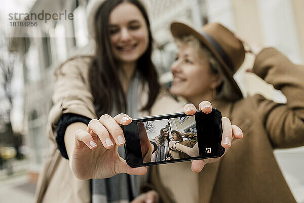 Tochter zeigt ihr Selfie mit Mutter auf dem Smartphone-Bildschirm