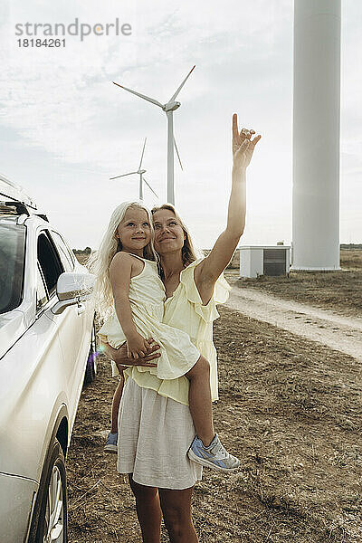 Lächelnde Frau gestikuliert und steht mit ihrer Tochter im Auto im Windpark