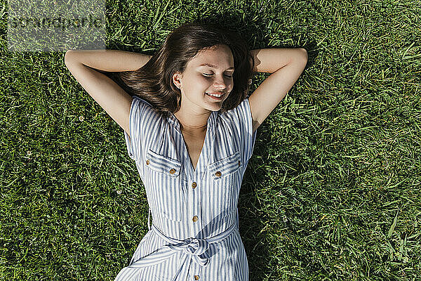 Happy young woman with eyes closed relaxing on grass