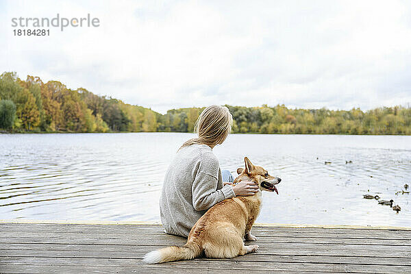 Frau mit Hund blickt am Steg auf den See