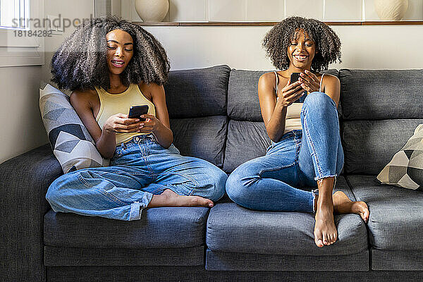 Junge Freunde sitzen auf dem Sofa im Wohnzimmer und nutzen Smartphones