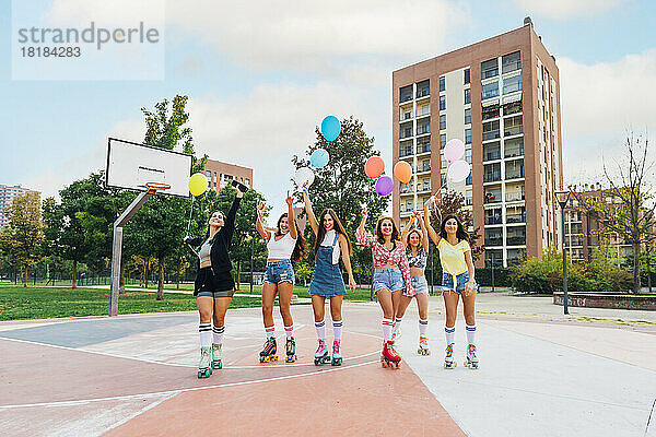 Fröhliche Freunde mit Luftballons stehen auf dem Basketballplatz