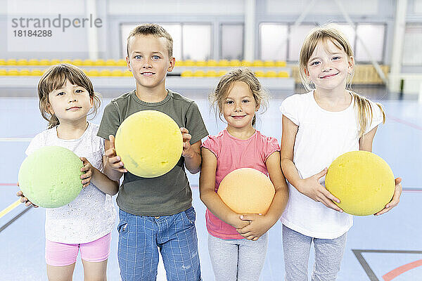 Lächelnde Grundschüler mit Ball stehen nebeneinander auf dem Schulsportplatz
