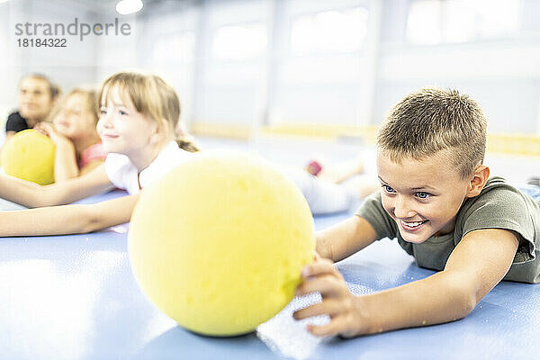 Smiling elementary boy looking at ball lying down at school sports court