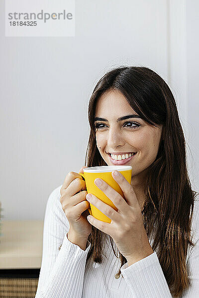 Lächelnde Frau hält Kaffeetasse zu Hause