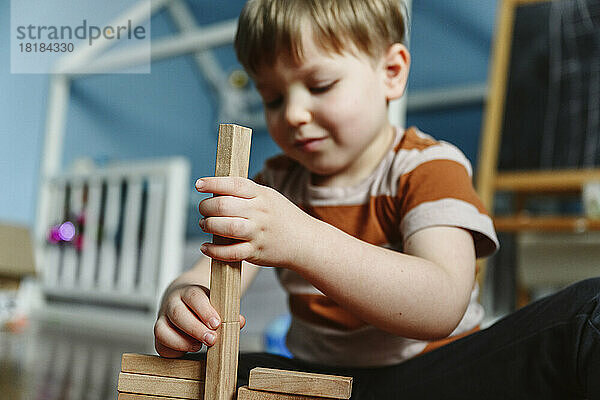 Lächelnder Junge spielt mit Holzklotz im Schlafzimmer zu Hause