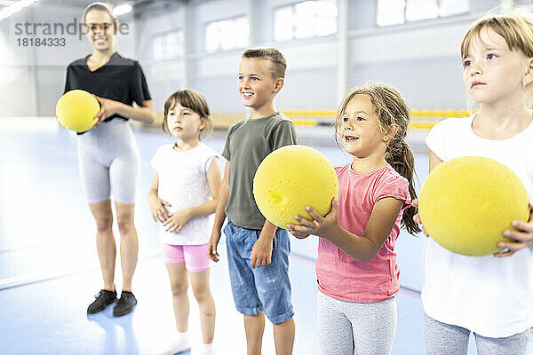 Lächelnde Schüler halten Ball  während der Lehrer am Schulsportplatz steht