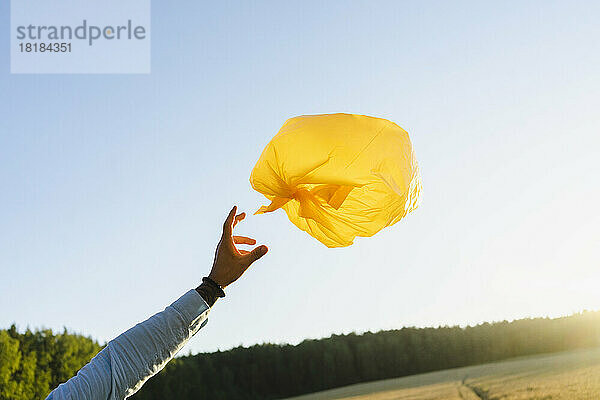 Hand of man reaching towards garbage bag balloon at field